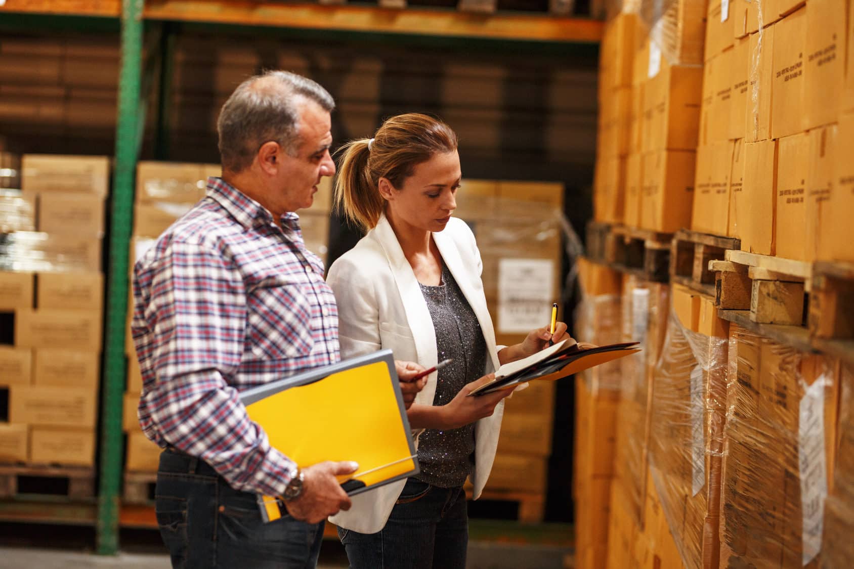 Female manager and warehouse worker checking list and inventory on the shelf in storehouse.